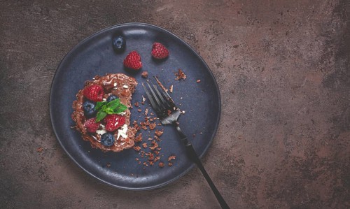 Half-eaten chocolate tartlet, on a plate, stuffed with cottage cheese and berries, breakfast,