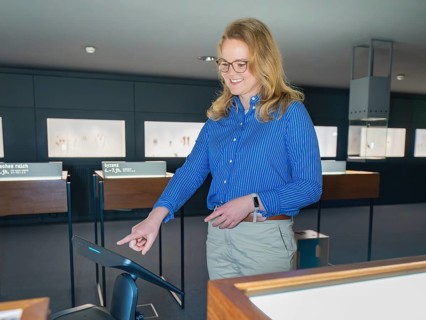 A woman in a blue shirt smiles and uses a digital screen in a museum, robotic personality