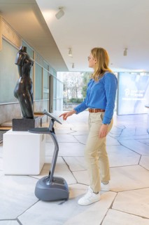 Woman using a device in front of a statue in a modern museum, robotic personality Roboloutions in