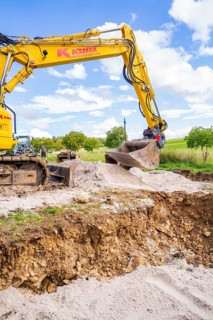 Excavator lifts soil on a construction site under a blue sky, Bau PV Freifaechenanlage, Weil der