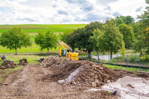 Excavator on a construction site with large mounds of soil in a green landscape, Bau PV