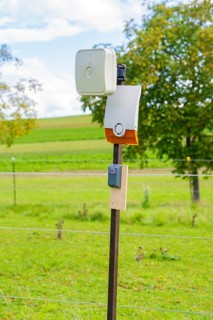 Camera mounted on a fence post in a rural landscape in front of a green field, Bau PV