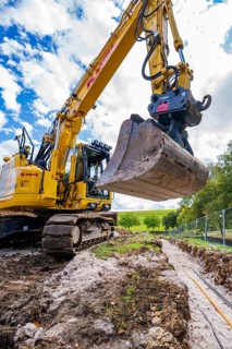 Large excavator digging a trench under cloudy sky, Bau PV Freifaechenanlage, Weil der Stadt,