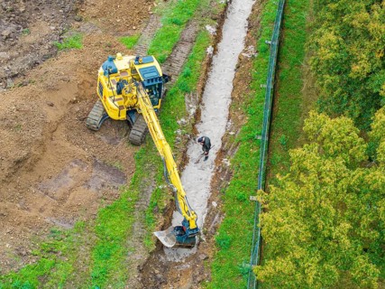 Excavator and construction worker at a ditch on a construction site, Bau PV Freifaechenanlage, Weil