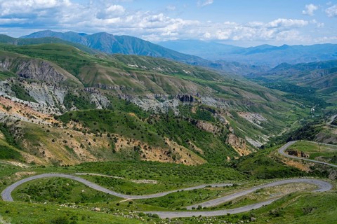 A winding road winds through the green mountains under a blue sky, view from Vardenyats Pass or