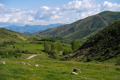 Mountainous valley with green meadow under a blue sky with clouds and power lines, landscape from