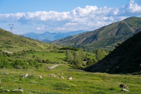 Valley with green landscape, power lines, surrounded by mountains and under a cloudy sky, landscape