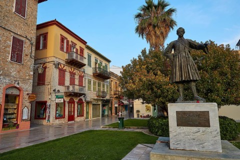 Old town of Nauplion, historical statue in a cozy street surrounded by old buildings and palm