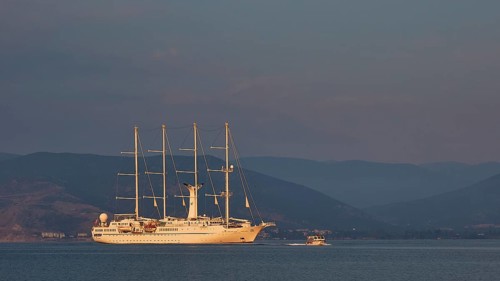 An illuminated sailing ship on calm water with mountains in the background at dusk, Nauplion,