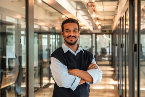 Young confident professional black man smiling and standing with crossed arms in a modern office or