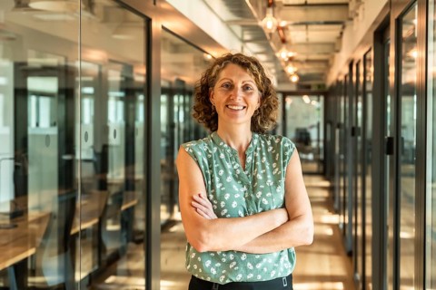 Professional woman with curly hair and arms crossed, confidently standing in a well lit modern