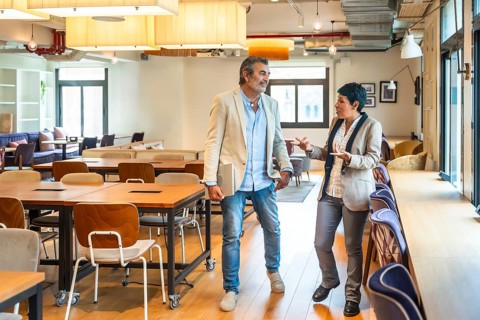 Diverse business professionals walking, talking, and discussing work in an open plan office,