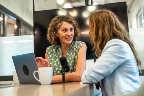 Two professional women collaborating on a podcast, recording a conversation with a microphone and