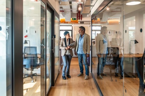 Two diverse business colleagues, a man and a woman, walking along a glass walled corridor in a