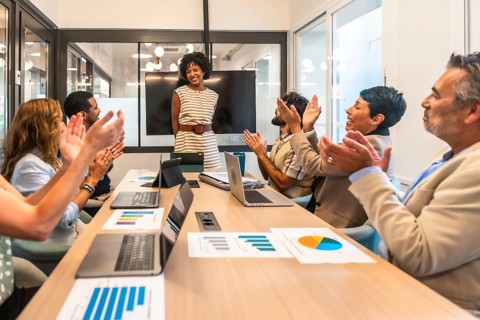 Diverse business professionals applaud a smiling female leader at a conference table after her