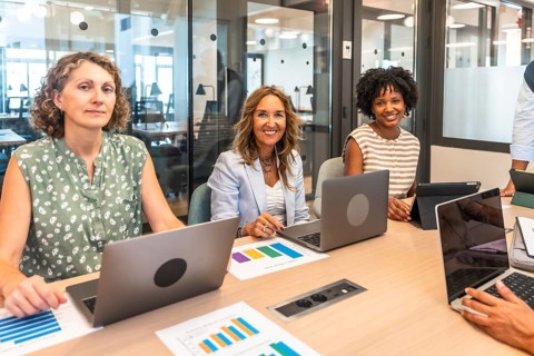 Diverse businesswomen are smiling at the camera, working with laptops and analyzing data graphs