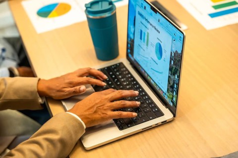 Person working on a laptop, hands typing on the keyboard, with a monthly performance review screen