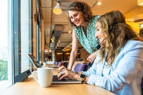 Two smiling women are collaborating and supporting each other while wearing headsets, working on