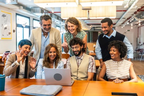 Diverse business colleagues collaborating and smiling during a video call on a laptop in a modern