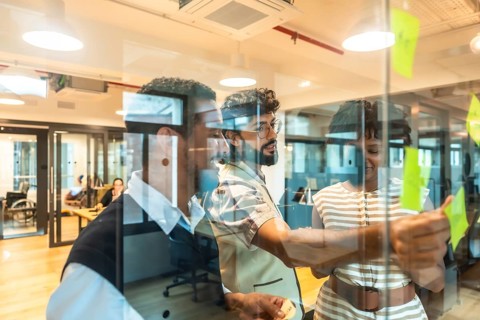 Business colleagues collaborating on a project, writing ideas on sticky notes affixed to a glass