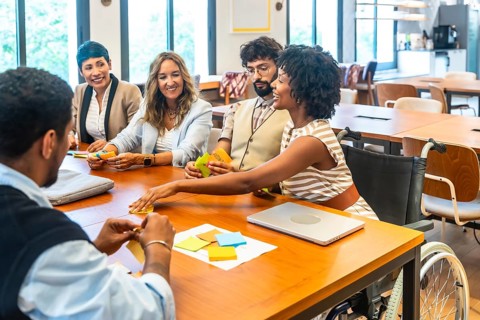 Diverse business team, including a woman in a wheelchair, collaborating around a wooden table in a