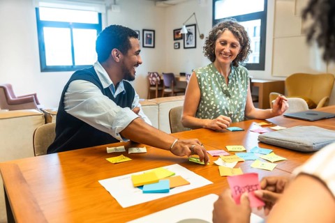 Diverse coworkers sitting around a wooden table, smiling and collaborating on new project ideas