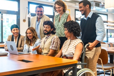 Diverse corporate team smiling and collaborating around a laptop in an inclusive coworking office,