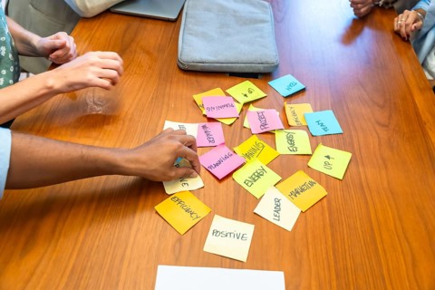 Diverse business colleagues collaborate around a wooden table, arranging colorful sticky notes and