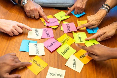 Business colleagues gathered around a wooden table point at colorful sticky notes labeled planning,