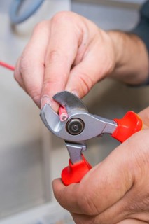Electrician uses pliers to cut red wire close-up