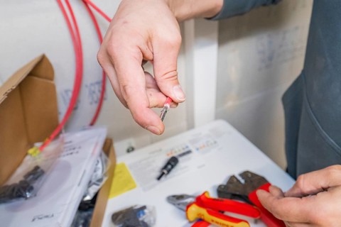 Electrician holds a small piece of cable in his hand, next to tools on the table