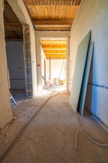 A shell with sunlight in the corridor. Cables, unfinished walls and a wooden floor define the room