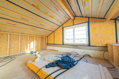 Unfinished construction of an attic with insulation on the walls. Large windows let in lots of