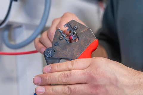 Hand holding pliers that process a cable, industrial environment