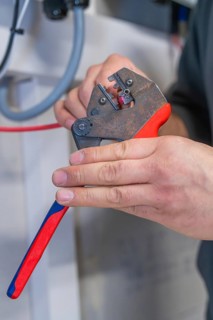 Electrician processes cables with pliers, workshop environment