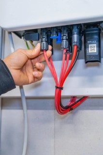 Hand connects several red cables to plugs in a control cabinet