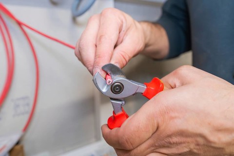 Close-up of a hand cutting a cable with pliers