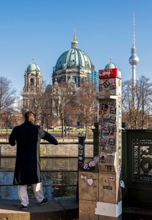 A man stands next to a demolished modern Telekom telephone column, view of Lustgarten Cathedral,