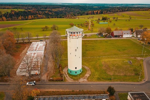 Water tower in the middle of a vast landscape with fields and small buildings in the background,