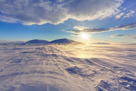 Midnight sun over windswept snow covered Arctic landscape at Mohnbukta, bay at western shore of