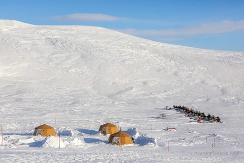 Snowmobiles, snow scooters at Arctic expedition camp with tents protected by tripwire fence against