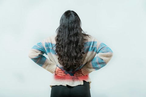 Suffering young woman with pain holding his back isolated. Female with spine problems isolated.
