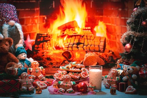 A plate of cookies and a glass of milk next to a Christmas tree and toys in front of a fireplace