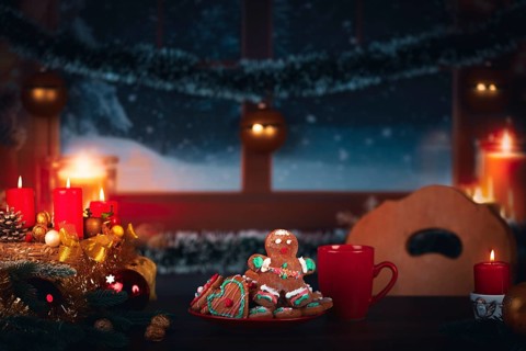 Christmas wreath with burning candles next to a plate with gingerbread in front of a window