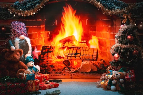 Fireplace with flickering fire surrounded by gifts and Christmas decorations, including teddy bears