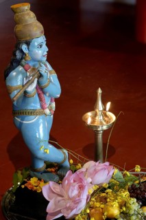 Sculpture of shepherd god Krishna playing his flute, fruits and vegetables lying on the ground,