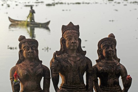 Three Hindu god statues made of clay, fishermen in a boat in the background, Vembanad Lake, Kerala,