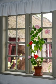 Geraniums in an old barred window and with a view out onto a half-timbered courtyard with a