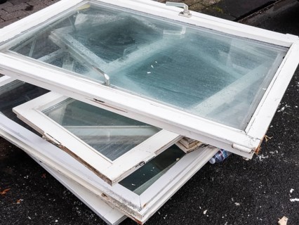 A pile of old white window frames with glass is lying on a sidewalk in Wuppertal, Germany
