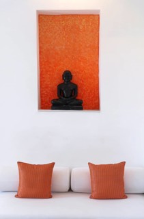 Statue of a black Buddha sitting meditating against an orange background, including bed with